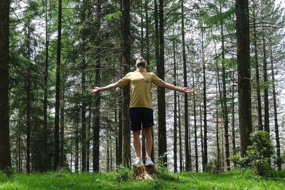 Holz muss atmen – en sportlicher Mann steht in einem Nadelwald und atmet tief ein.